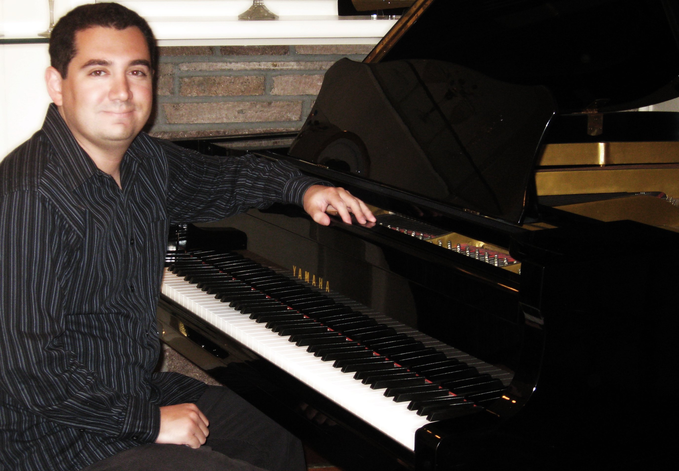 Jason Solowsky seated at his Yamaha grand piano at home, one hand resting on the fallboard above the keys