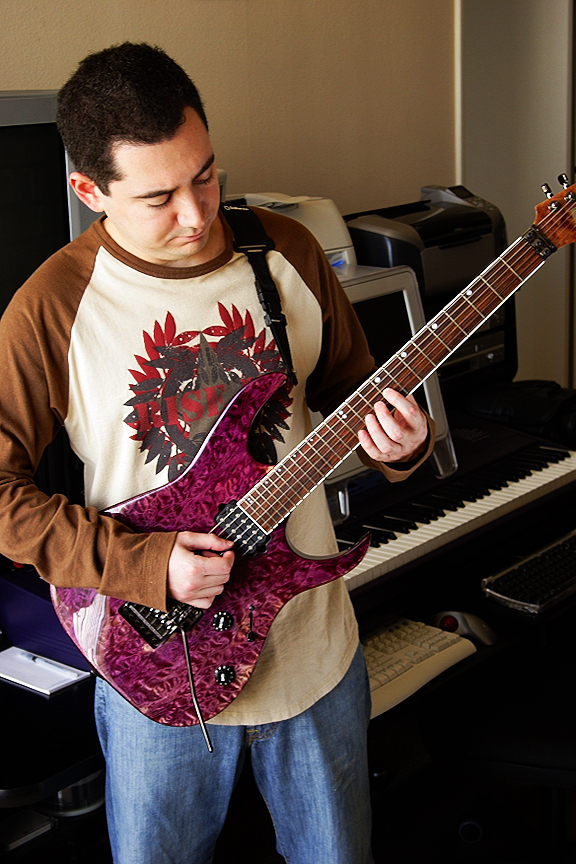 Jason Solowsky playing a purple electric guitar in his studio, with a keyboard behind him