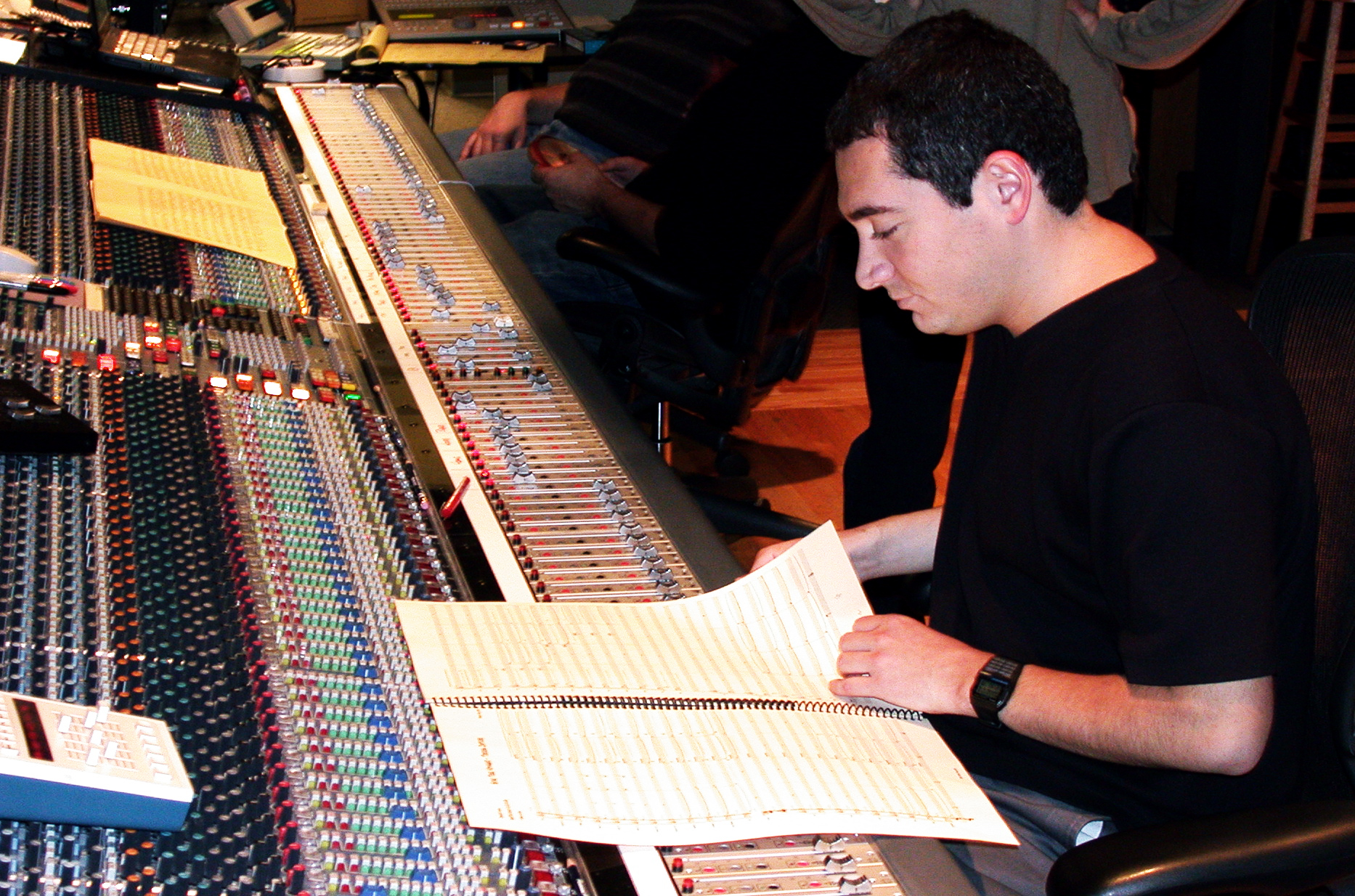 Jason Solowsky seated at a large mixing console, reading a score